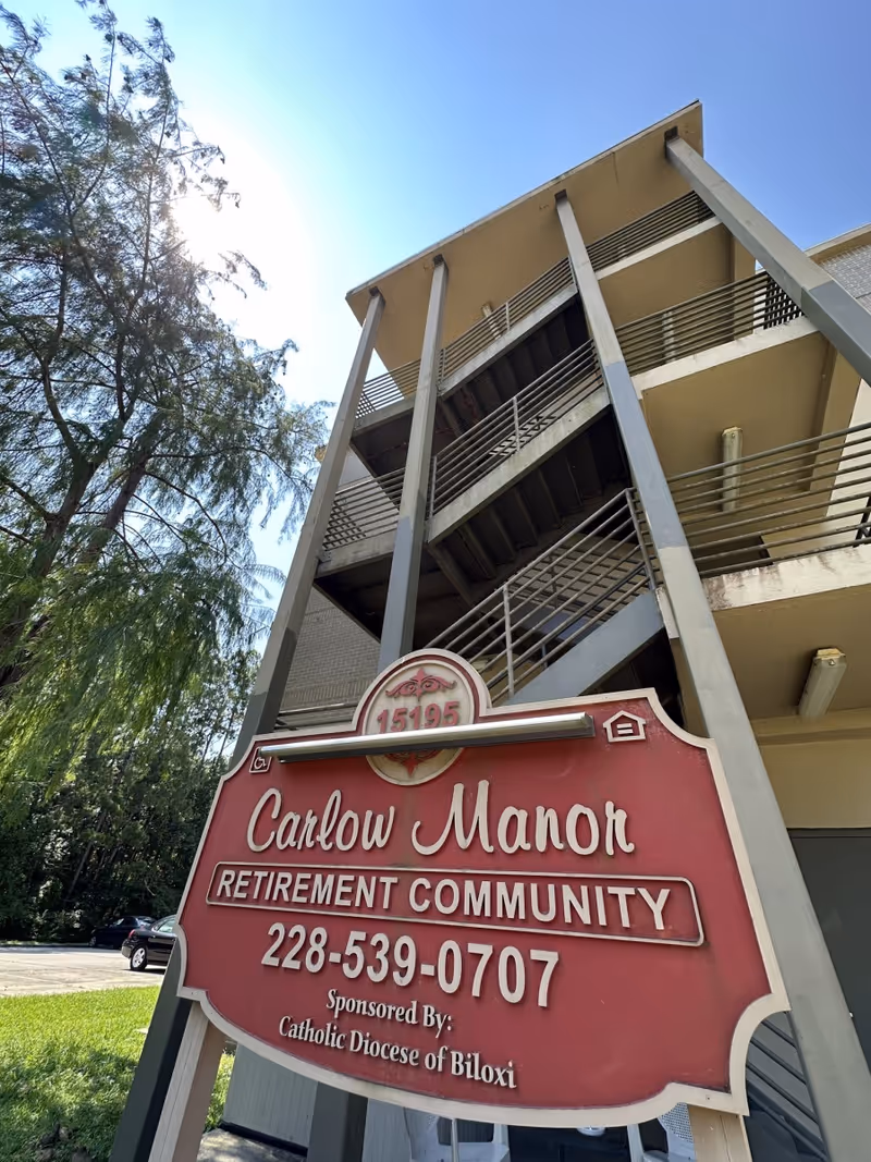Exterior view of Carlow Manor Retirement Community with a tall building and a red sign in the foreground.