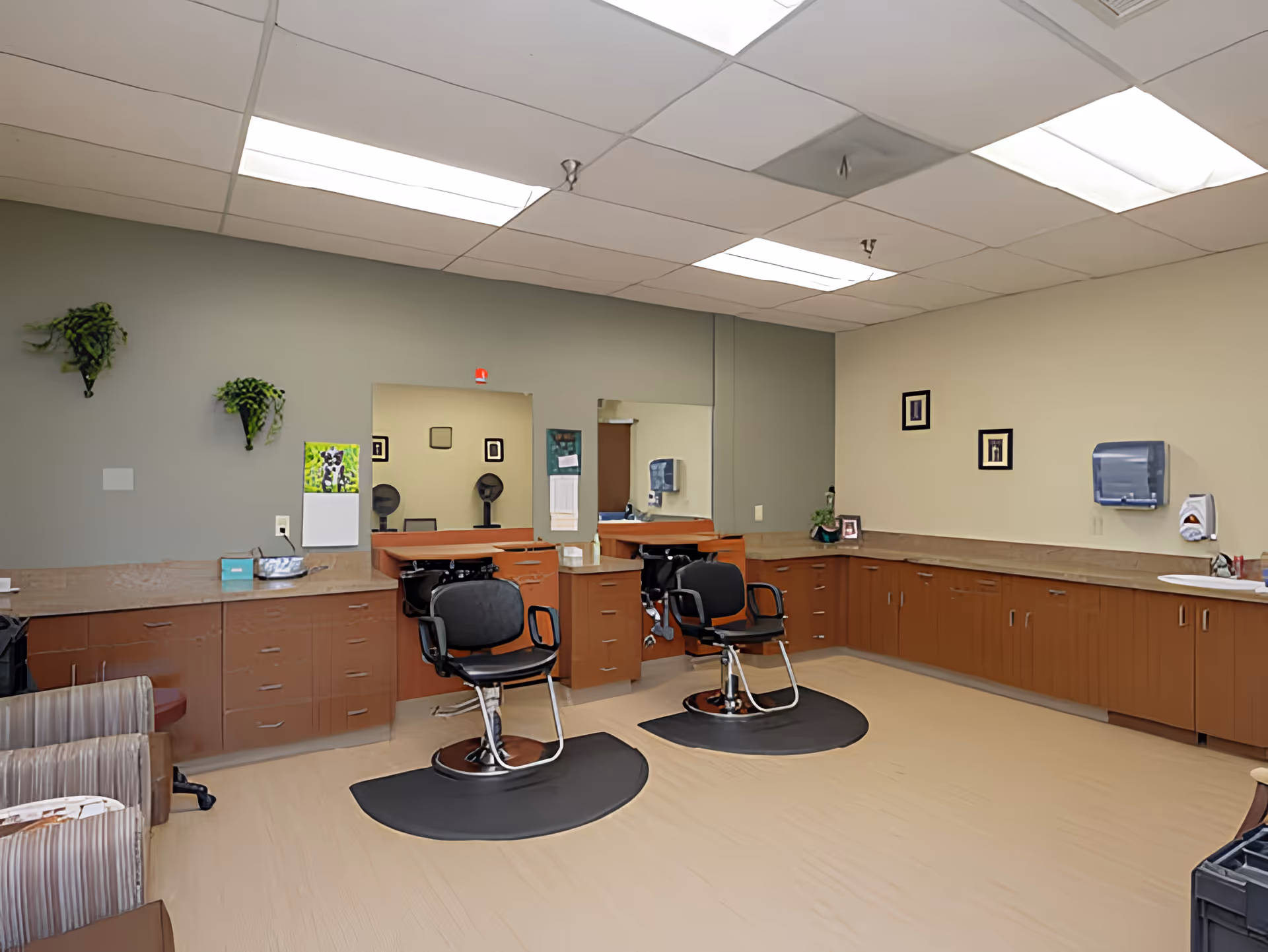 Bright salon-style room with two barber chairs, mirrors, and long wooden cabinets along the walls.