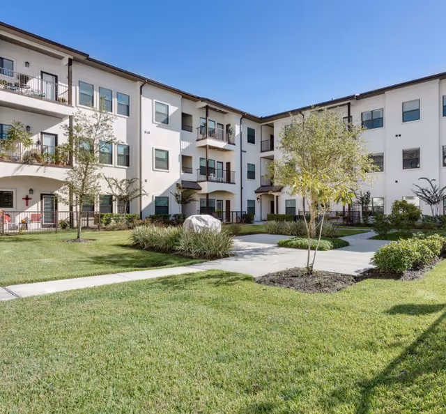 Exterior view of a white, multi-story senior living building with a manicured courtyard.