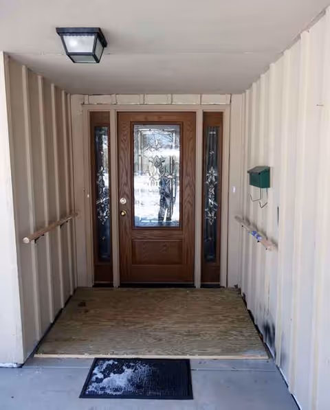 Front entry doorway with wood door, beige siding, handrails, and a small green mailbox.