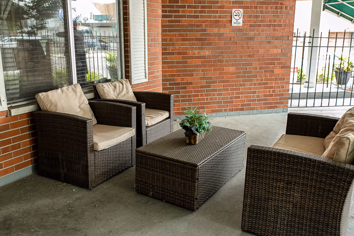 Wicker patio seating with cushioned chairs and a coffee table with a small potted plant on a covered brick porch.
