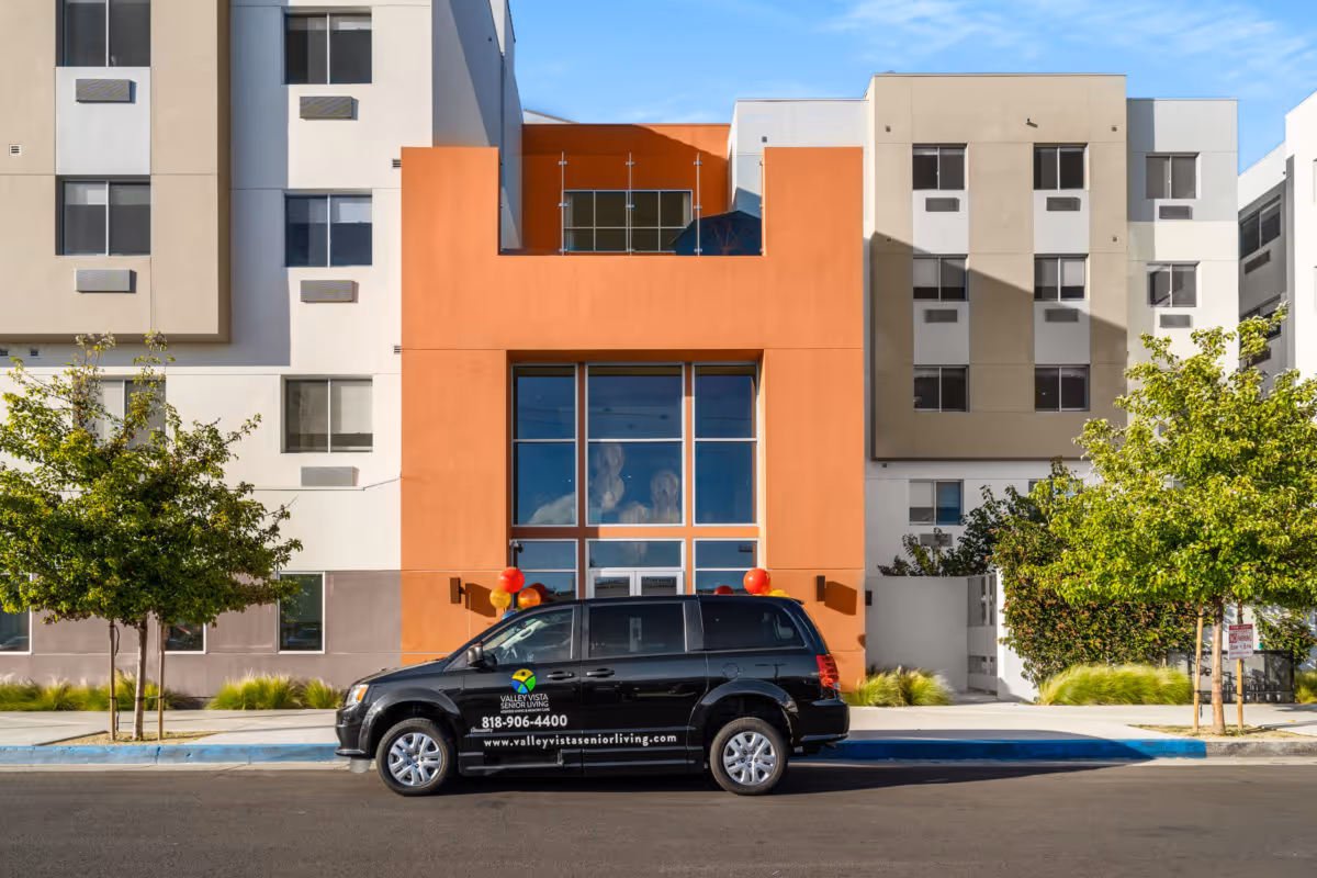 Modern multi-story senior living building exterior with a black Valley Vista Senior Living van parked in front.