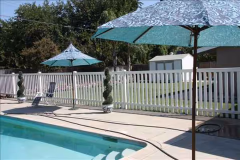 Outdoor pool area with lounge chairs and umbrellas behind a white fence.