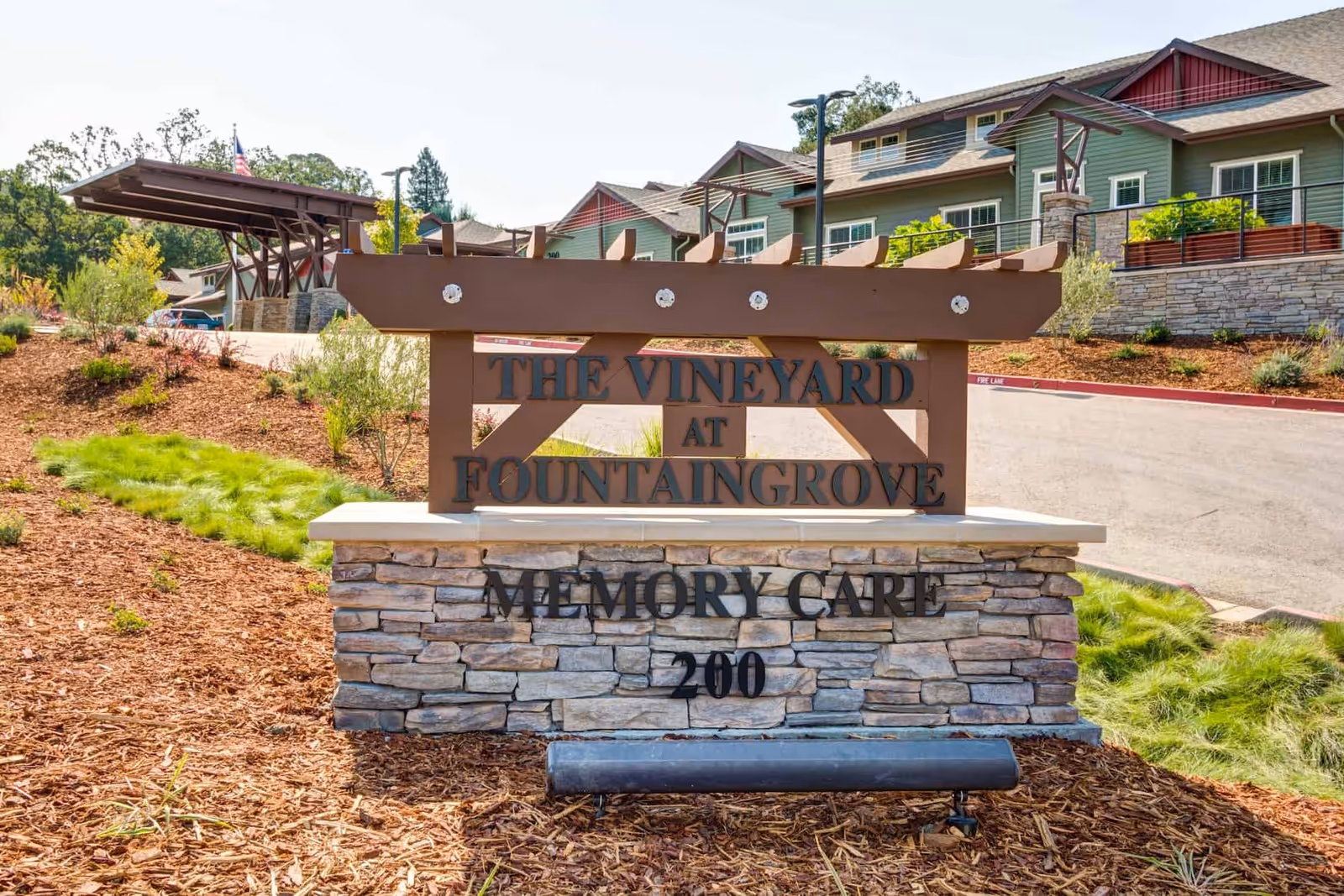 Stone and wooden entrance sign reading "The Vineyard at Fountaingrove Memory Care 200" in front of the facility building and landscaped entrance.
