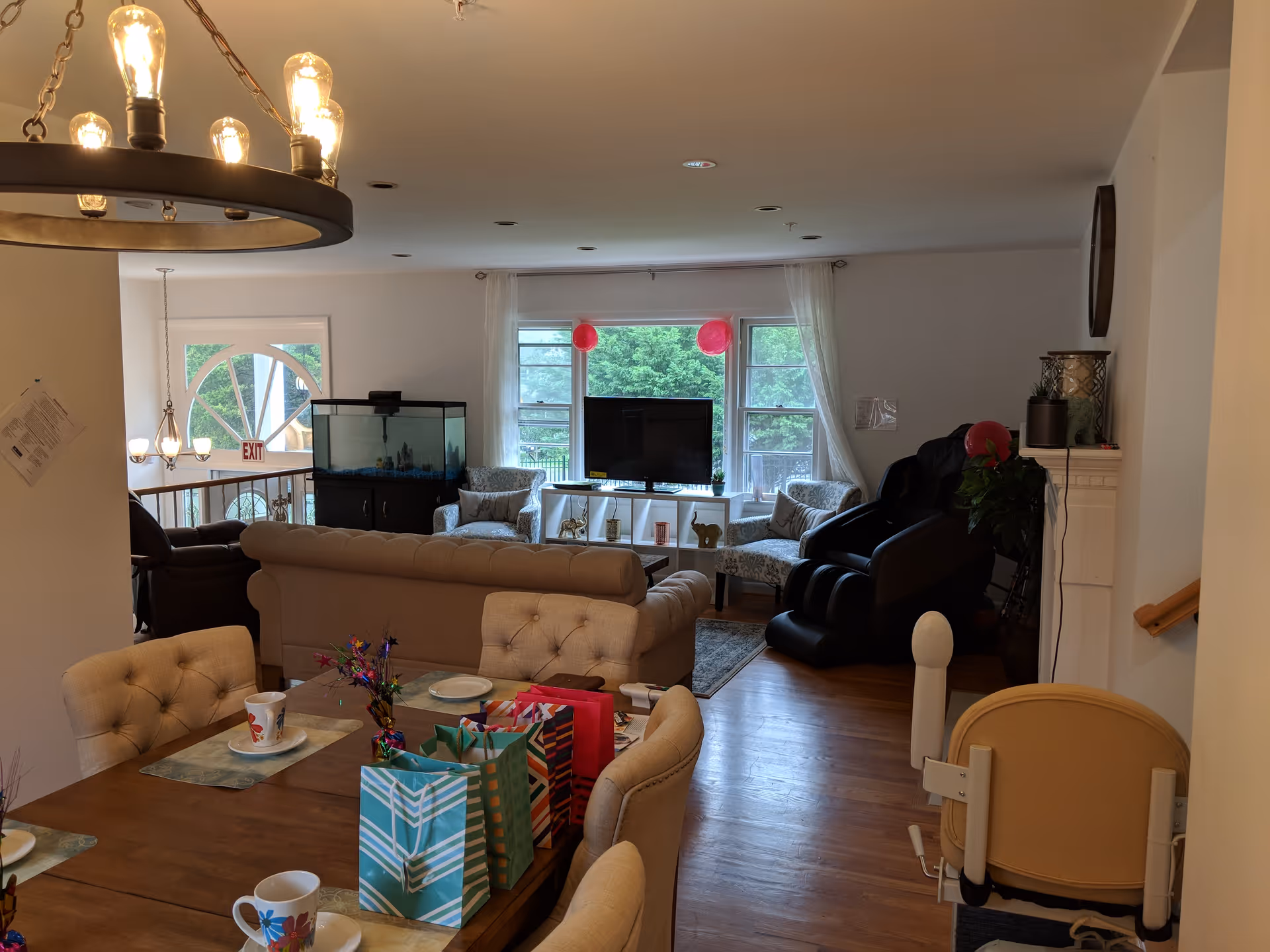 Open living room and dining area with a wooden dining table set with cups and gift bags, sofas and a TV, and a stairlift near the doorway.