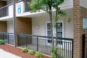 Ground-level apartment entrance with white double doors, a black metal railing, small tree and a 'Building B' sign.