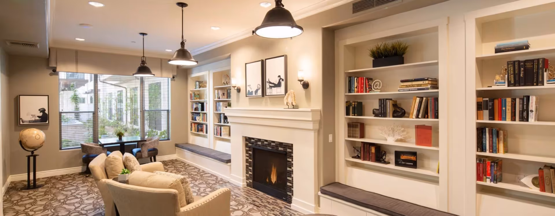 Bright lounge with armchairs, a fireplace, built-in bookshelves and window seating.