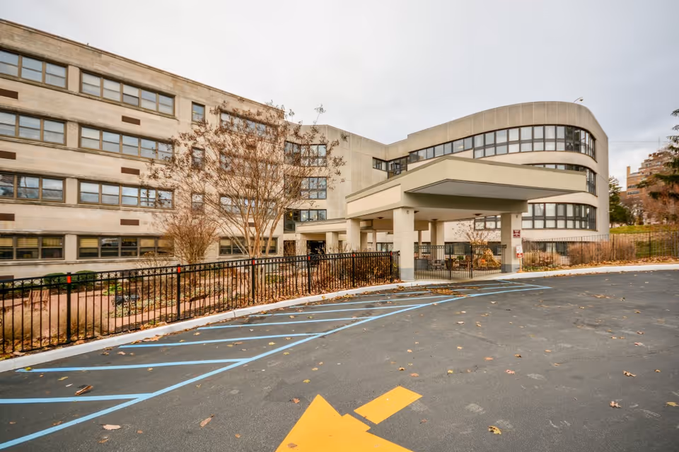Covered drop-off and driveway in front of a multi-story rehabilitation and healthcare building with large windows and parking spaces.