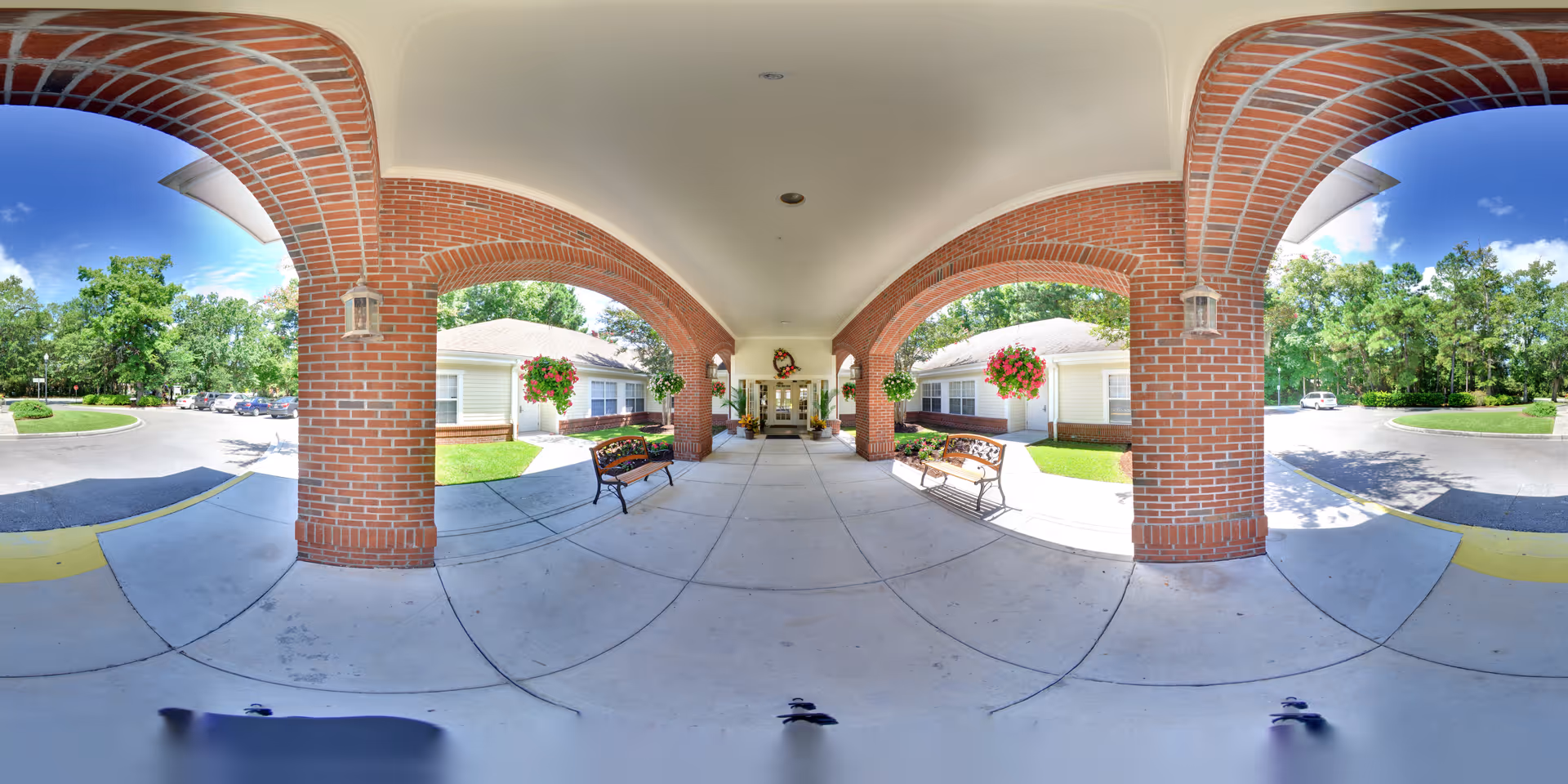 Covered brick-arched front entrance with benches, hanging flower baskets, and a driveway.