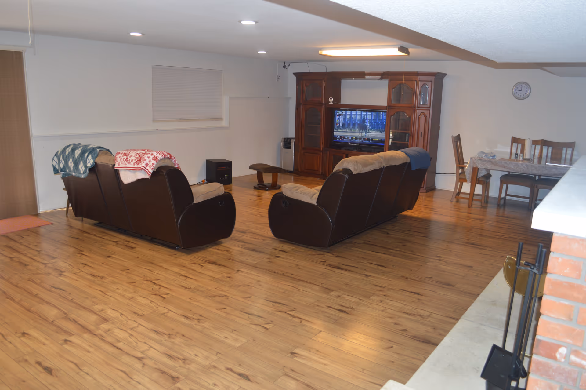 Spacious common living room with two brown recliner sofas facing a wooden entertainment center and TV, with a dining table in the background.
