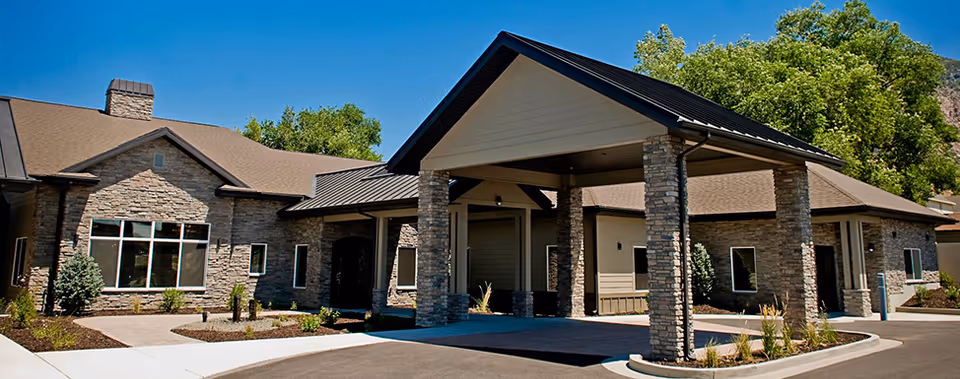 Single-story assisted living building with stone facade and a covered porte-cochere entrance, landscaped grounds and driveway.