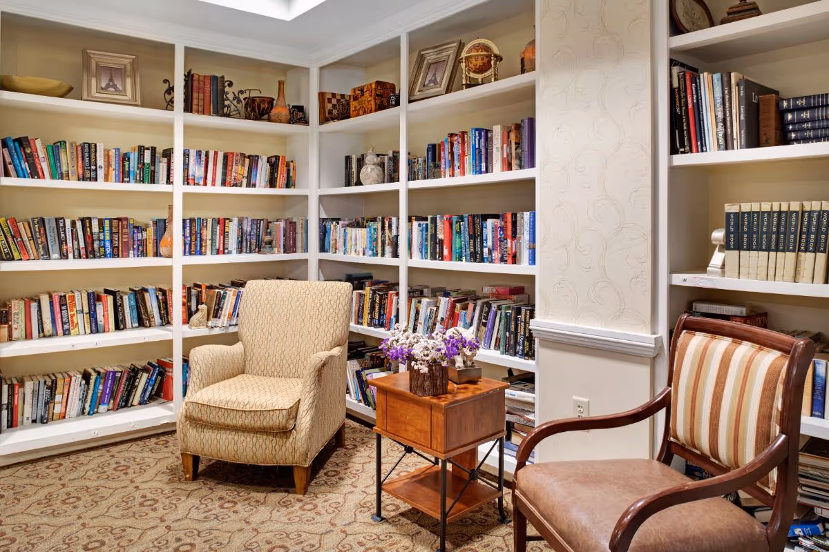 Cozy library corner with built-in bookshelves, two armchairs and a small side table with flowers.