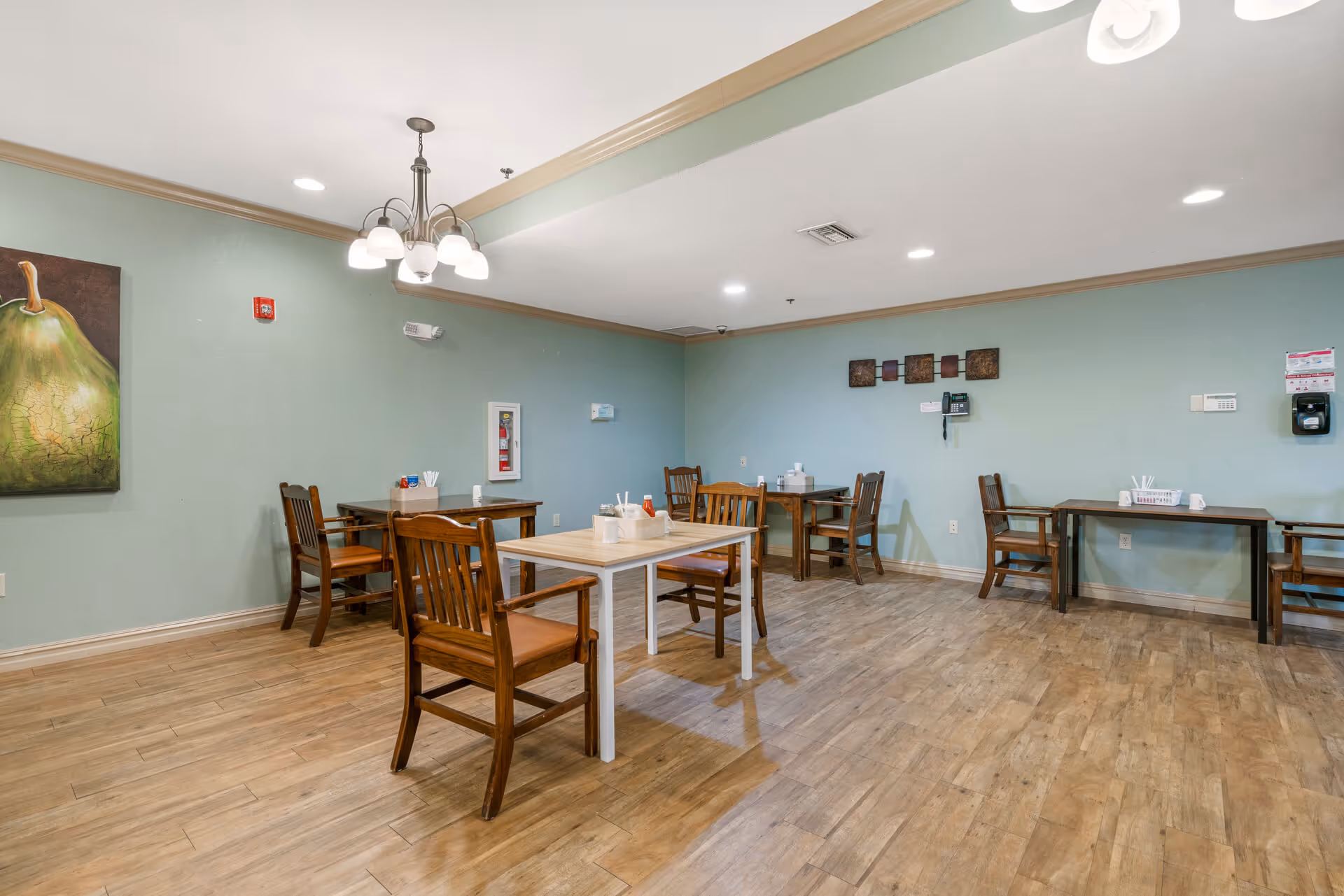Communal dining area with wooden tables and chairs, mint-green walls, and wood-look flooring.