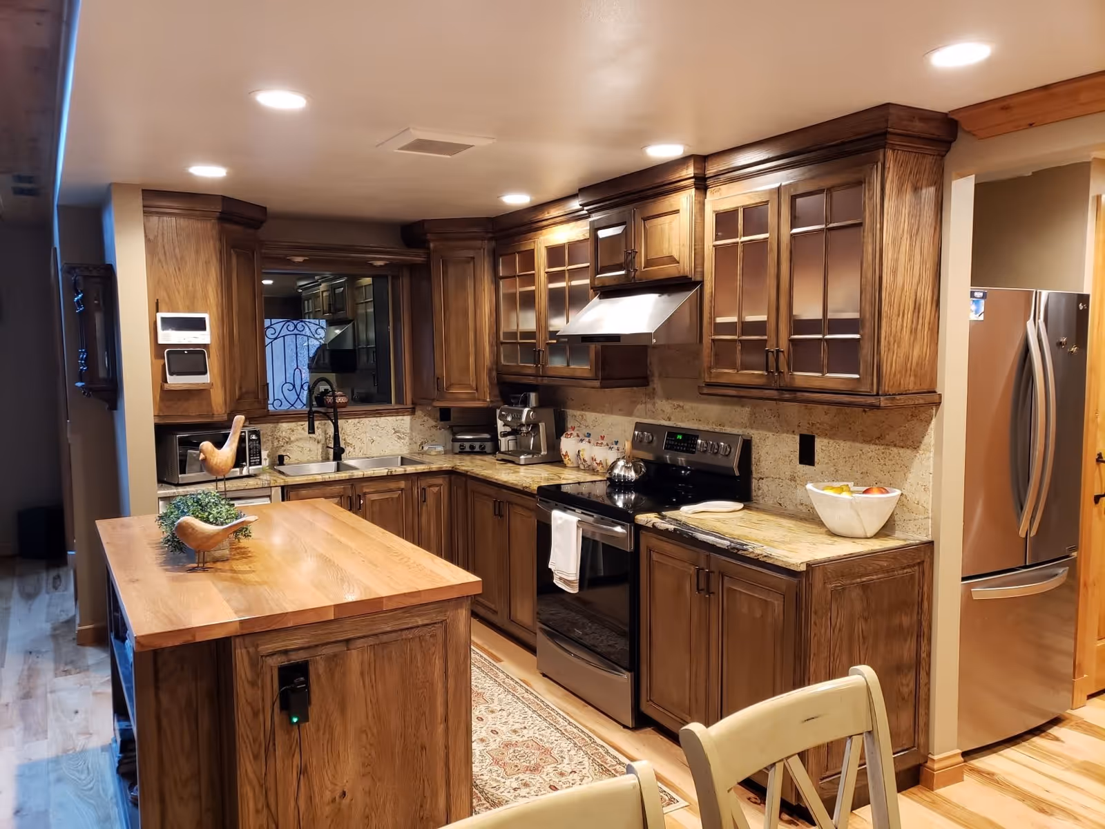 Well-lit kitchen with wooden cabinets, a central wooden island, stainless steel appliances, and granite countertops.