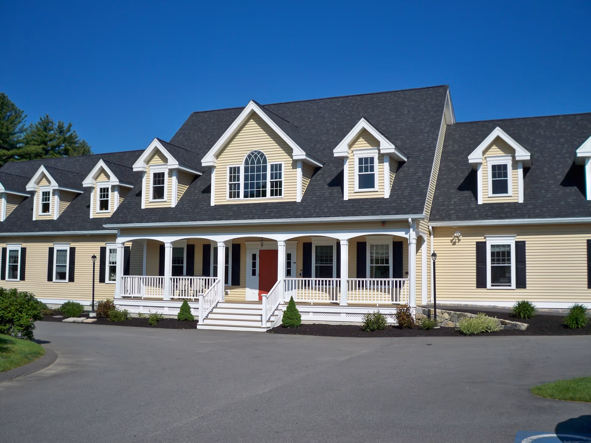 Front view of a beige, multi-wing senior living facility with a covered porch and dark roof.