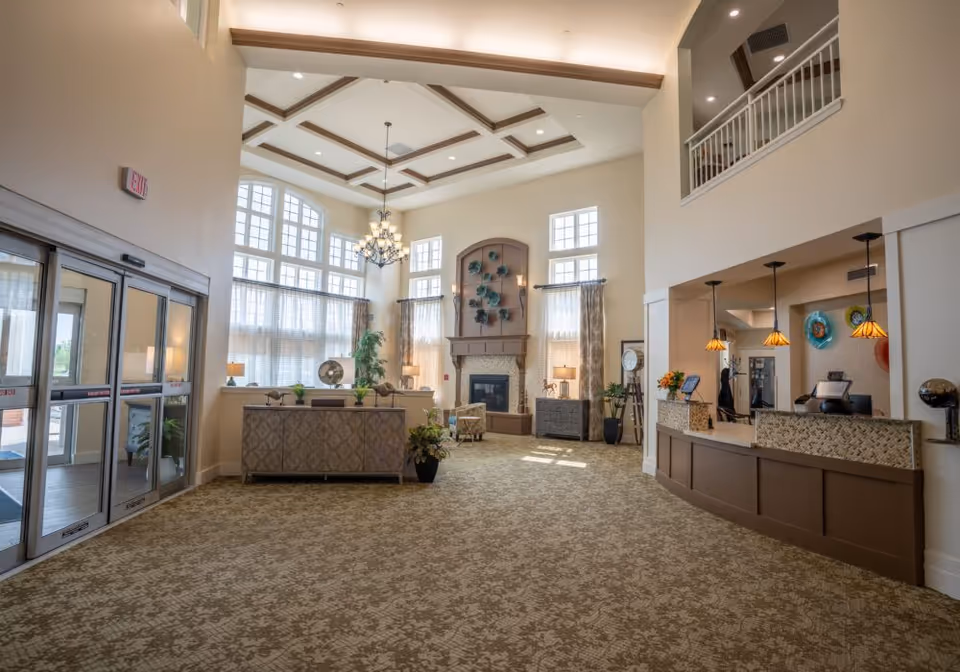 Spacious senior living lobby with high ceilings, chandelier, seating area, fireplace, and a reception desk.