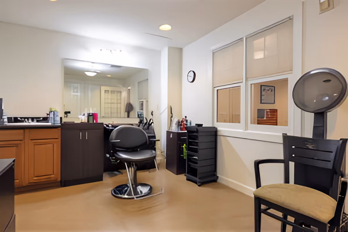 Interior salon-style room with styling chairs, a hooded hair dryer, cabinets and a large mirror.