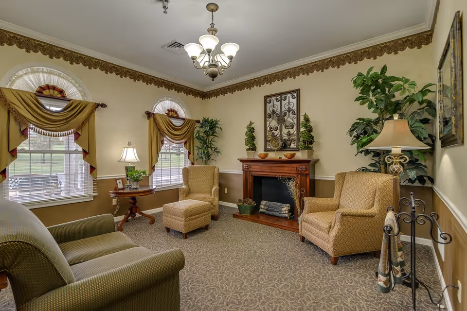 Cozy senior living sitting room with upholstered chairs, a fireplace, lamps, and decorative plants.