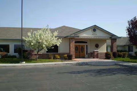 Front view of a single-story senior living building with brick pillars and a blooming tree.