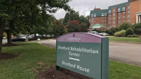 Outdoor view of Stratford Rehabilitation Center sign with red-brick building in background.