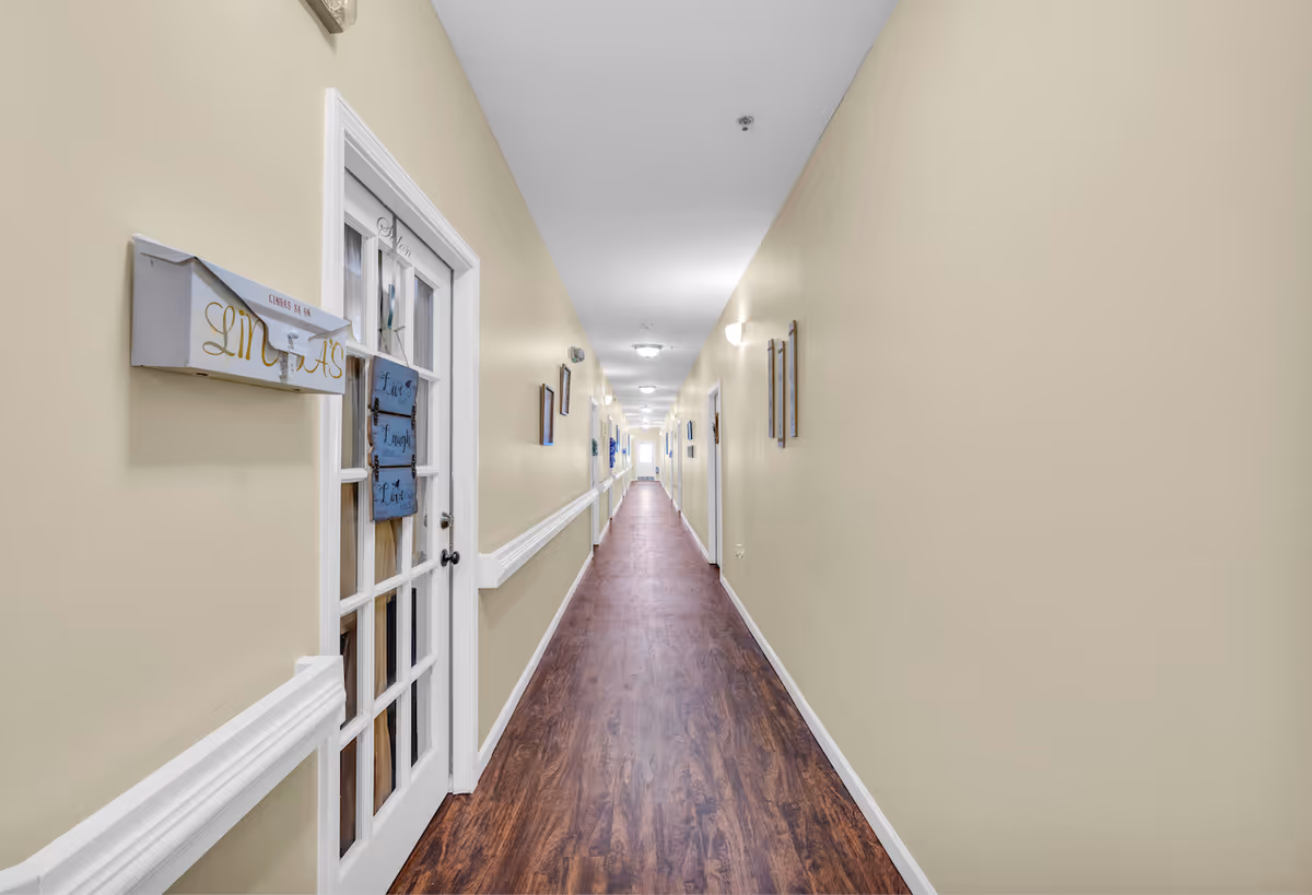 Long well-lit interior corridor with wood flooring, beige walls, white doors, handrails and wall decor.