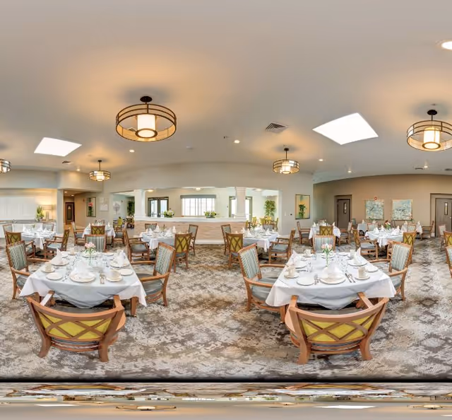 Spacious dining room with multiple tables set with white linens, place settings and wooden chairs beneath ceiling lights.