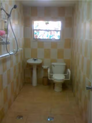 Small tiled bathroom with sink, toilet, grab bars, showerhead, and a window.