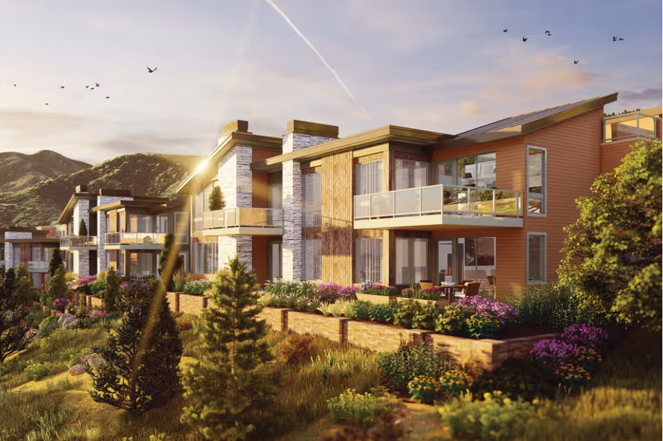 Exterior view of a modern senior living facility named Academy Mapleton Hill, featuring multiple two-story buildings with balconies, surrounded by landscaped gardens and greenery, set against a backdrop of hills under a partly cloudy sky with birds flying.