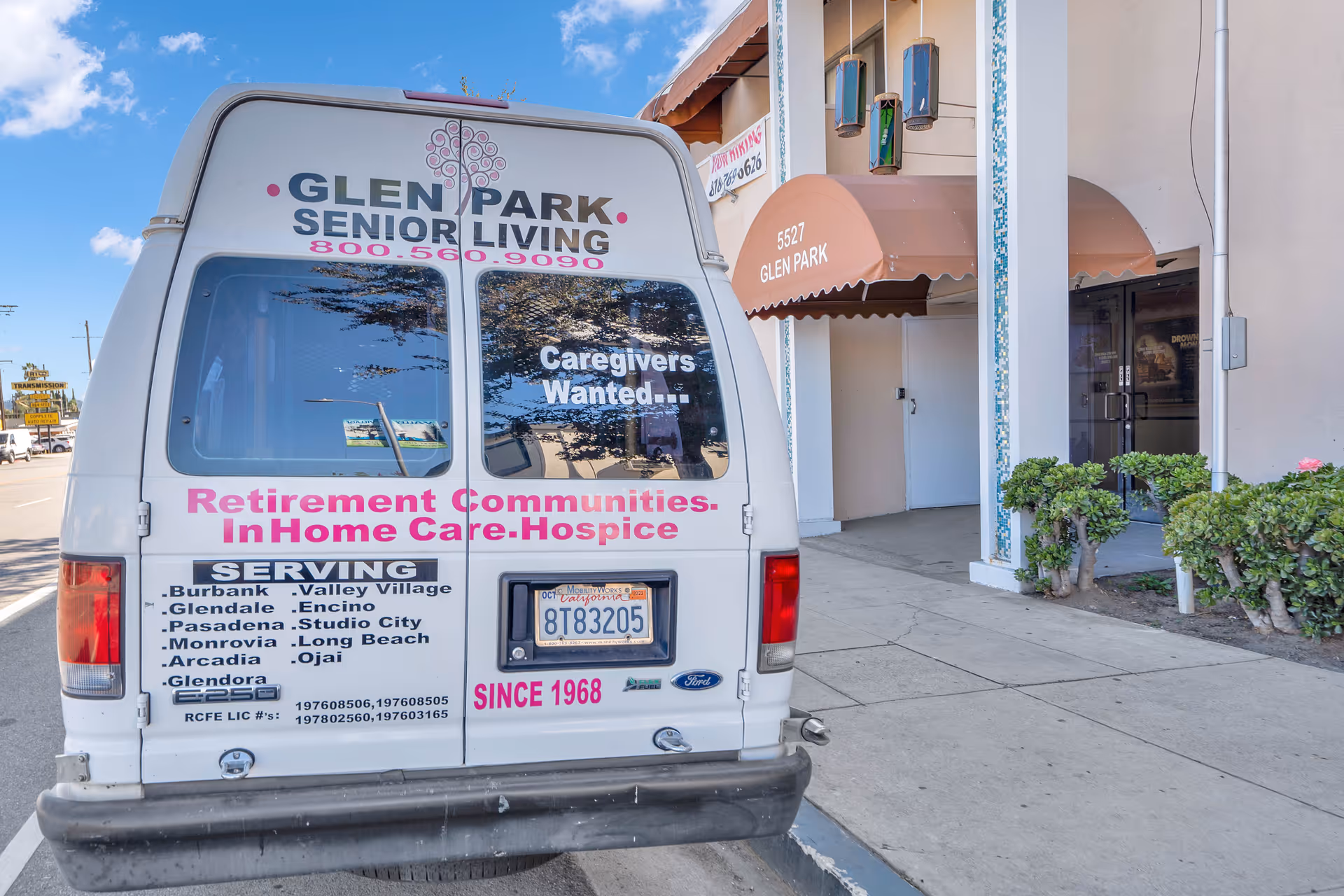 Rear view of a white Glen Park Senior Living van parked on the street near the entrance of a building with an awning labeled 5527 Glen Park. The van displays text advertising retirement communities, in-home care, hospice services, and caregiver job openings.