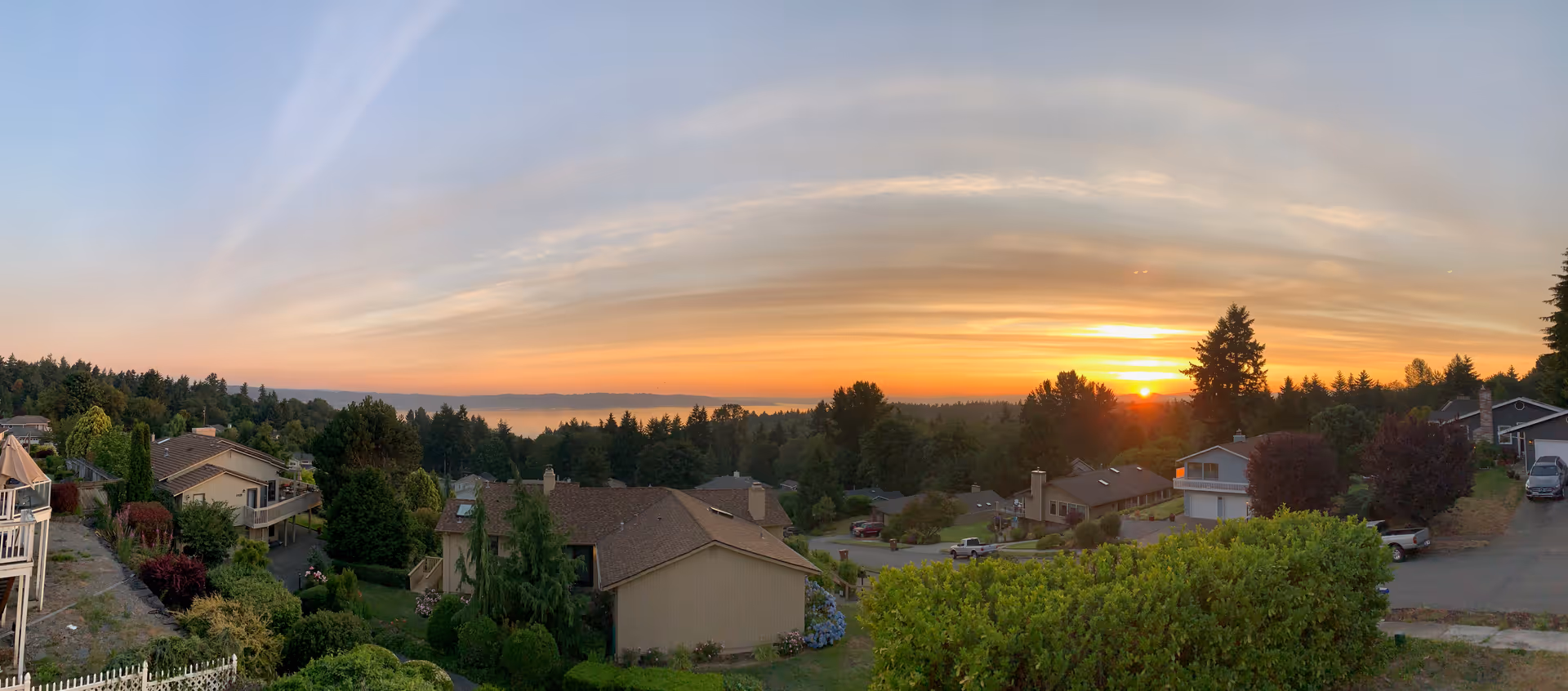 Panoramic view of a residential neighborhood at sunset with houses, trees, and a clear sky with soft clouds.