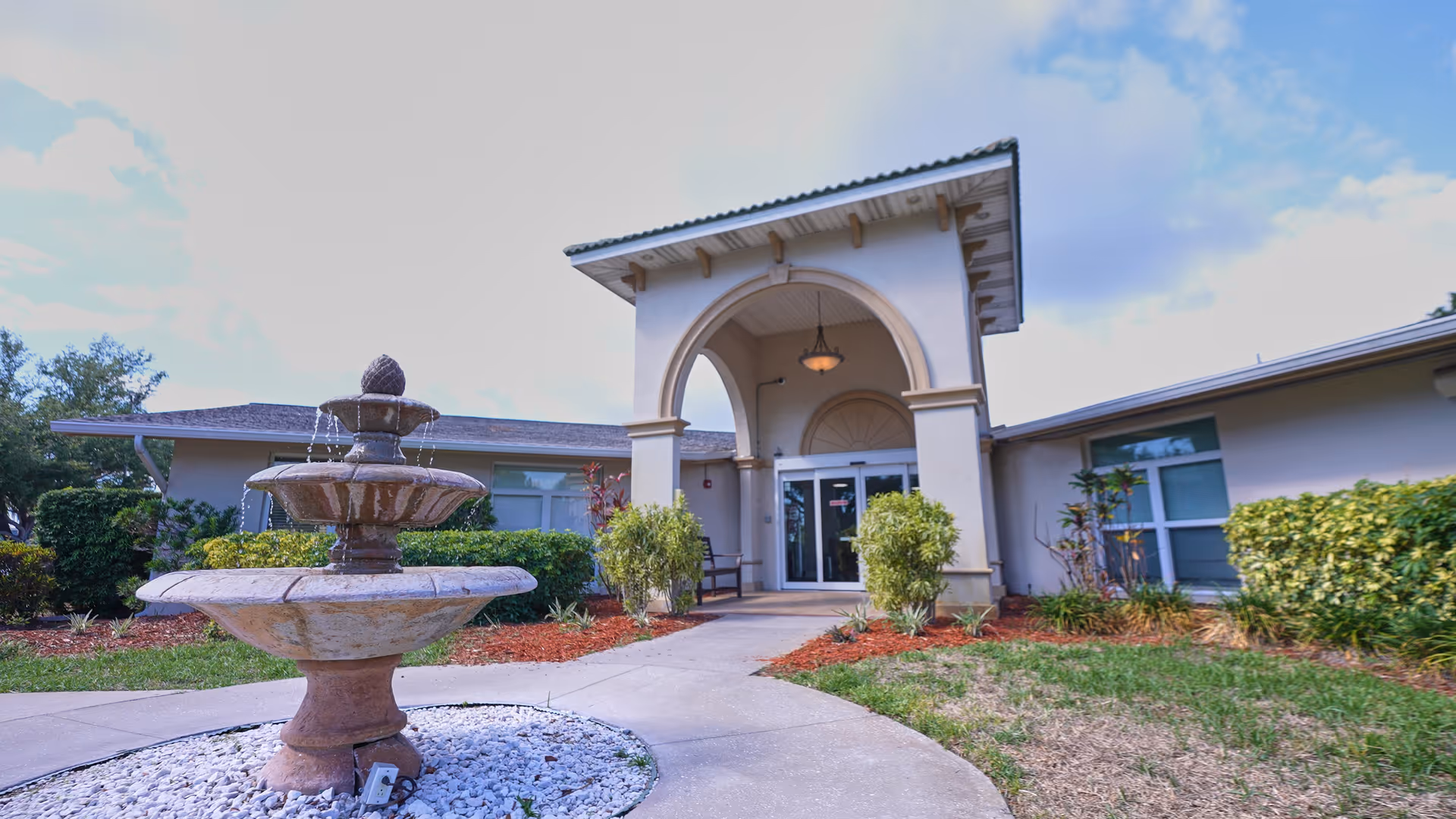 Front entrance of a nursing center with a three-tier stone fountain and an arched covered portico.