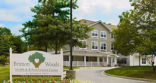 Three-story gray building with a curved driveway and a Brinton Woods sign at the entrance.
