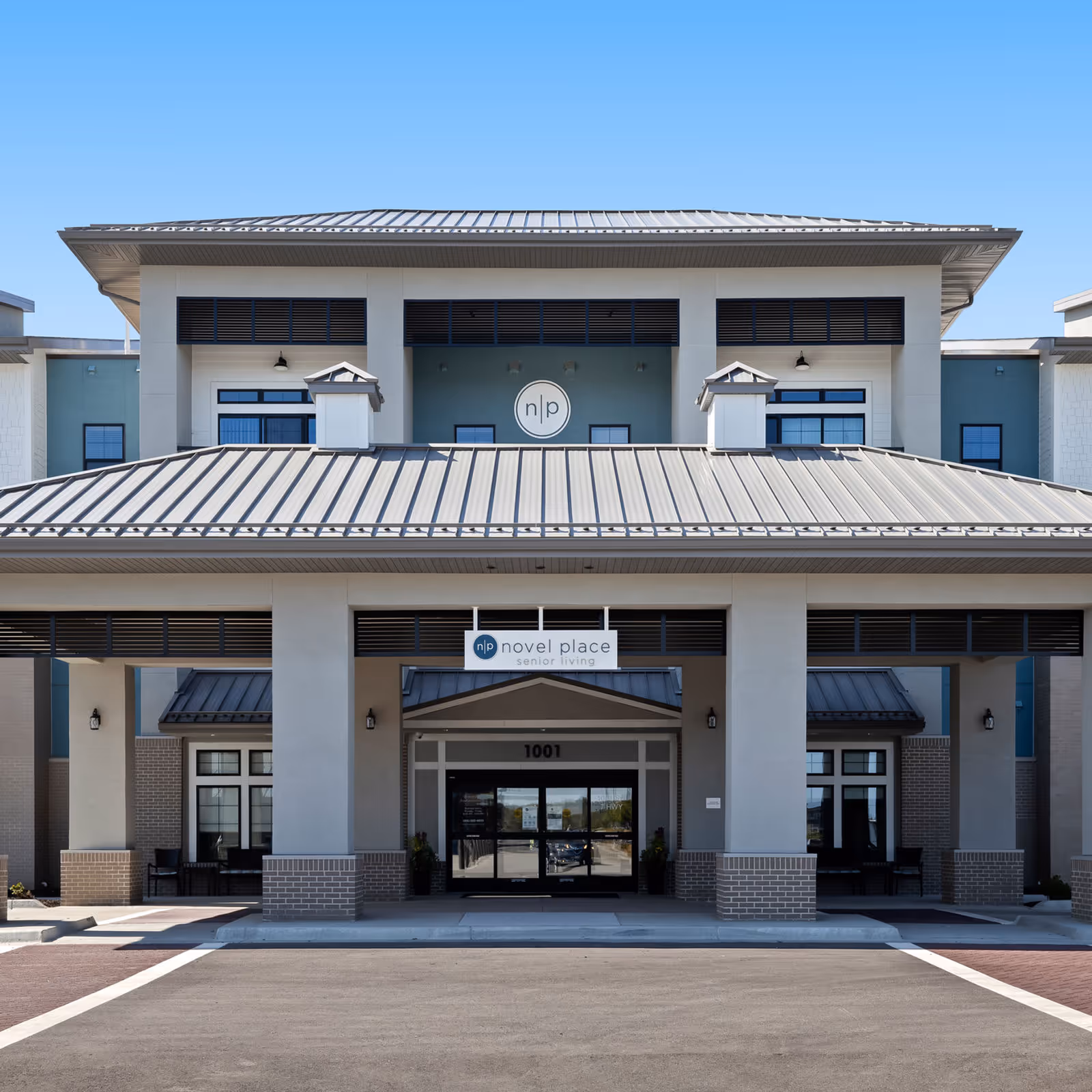 Front entrance of Novel Place Senior Living, a multi-story building with a covered porte-cochere, columns, and signage above the doors.