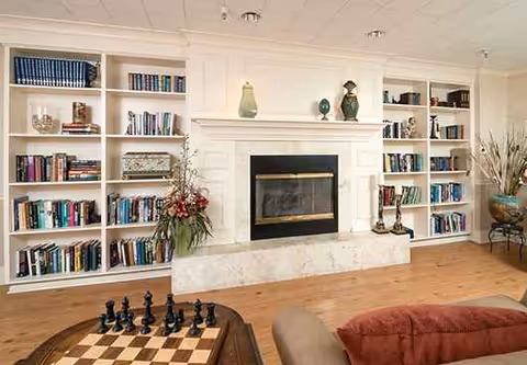 Bright living room with white built-in bookshelves around a fireplace and chessboard on a coffee table.