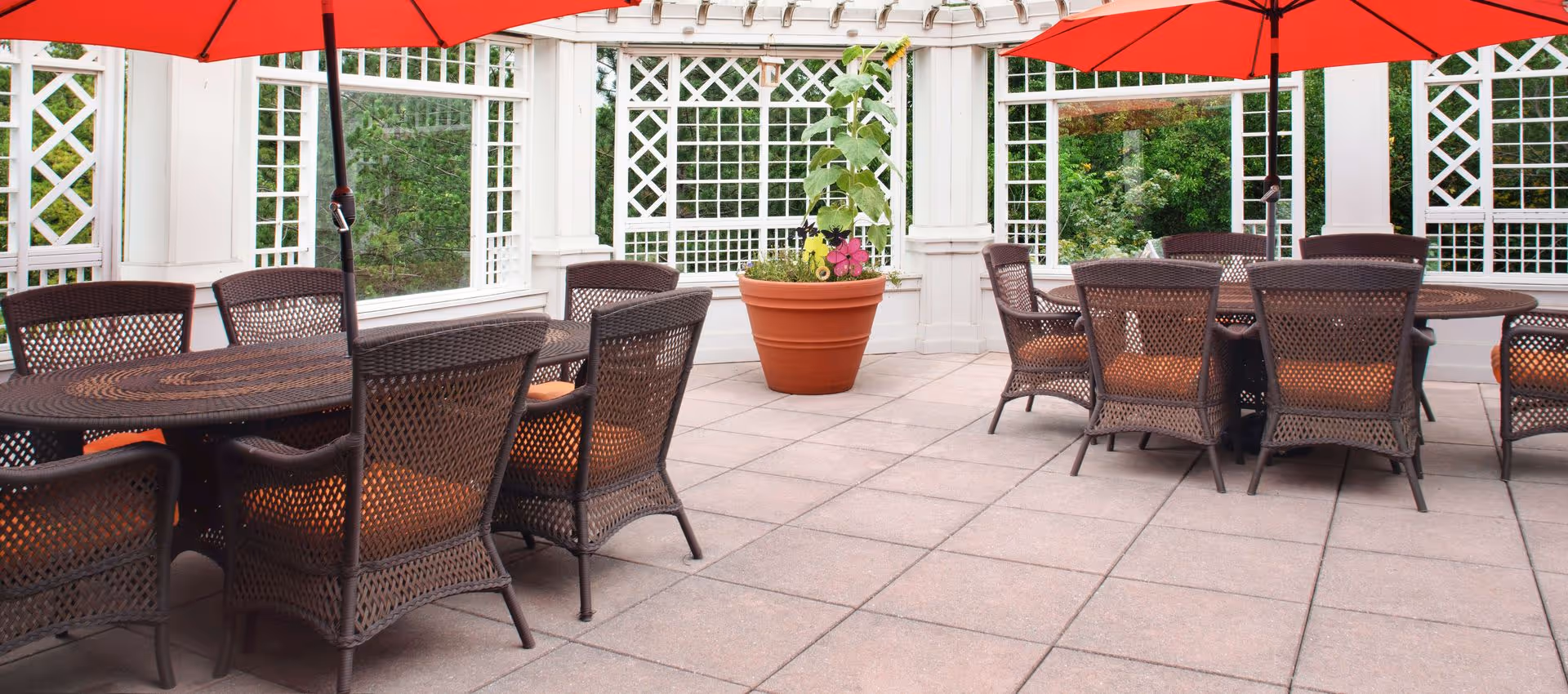 Outdoor patio with wicker tables and chairs under red umbrellas and a white lattice pergola.