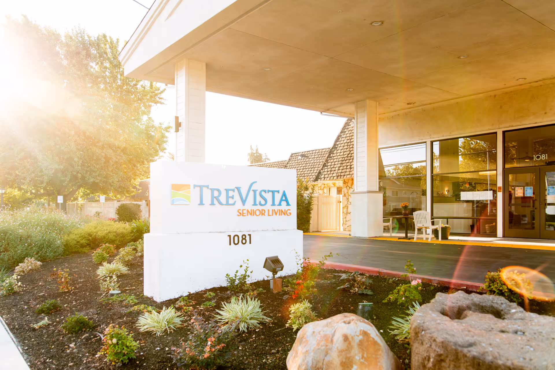 Covered entrance and landscaped front of TreVista Senior Living with a prominent white sign reading "TreVista Senior Living" and the address 1081.