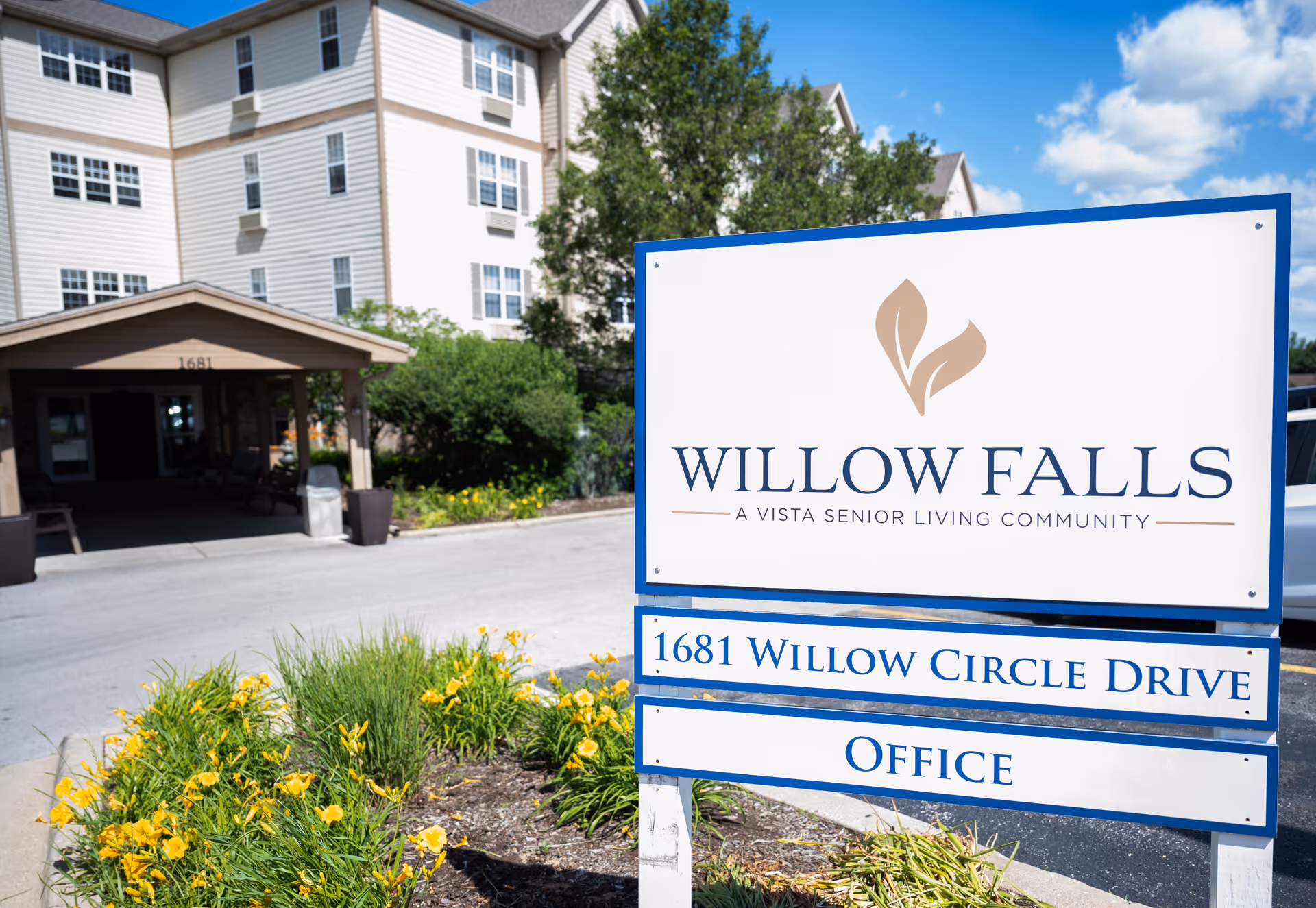 Sign for Willow Falls senior living in front of the facility entrance with landscaping and flowers.