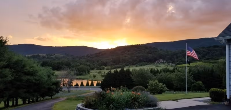 Sunset over hills behind a landscaped lawn and American flag at Acadia Care facility