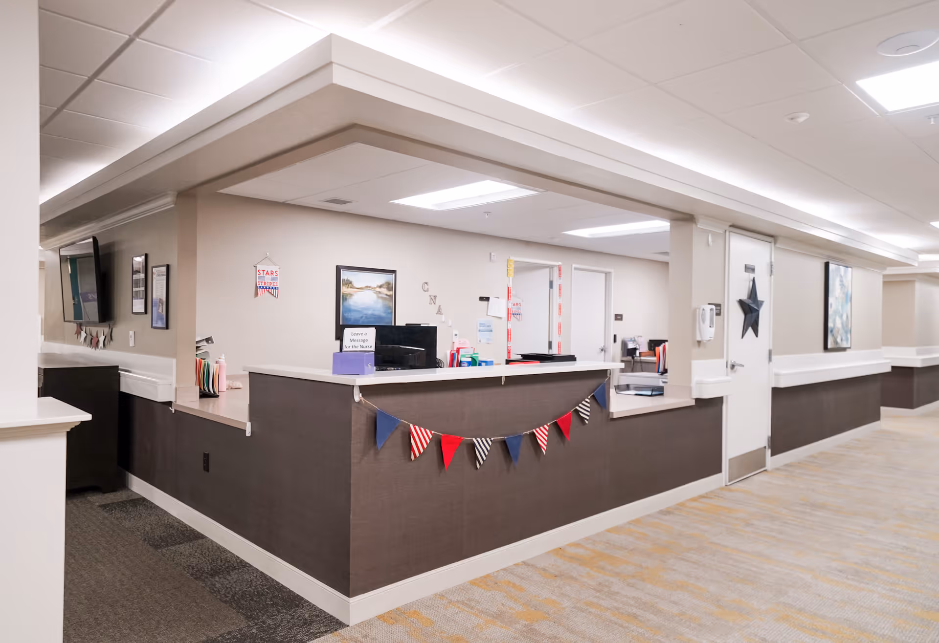 Nurse station reception desk in a bright, modern hallway of a senior living facility decorated with small pennant flags.