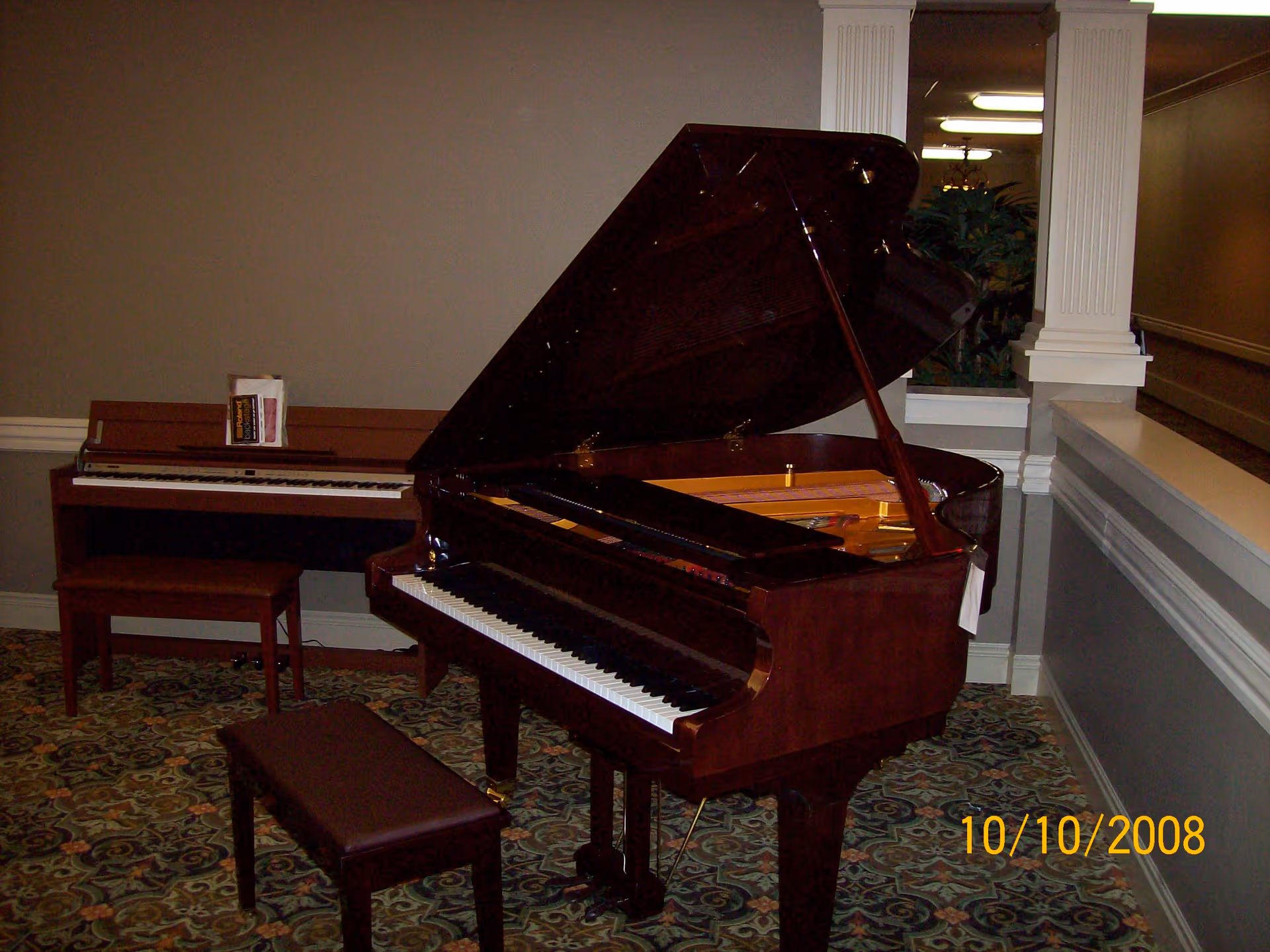 A grand piano with its lid open and an upright piano with benches in a carpeted interior room.