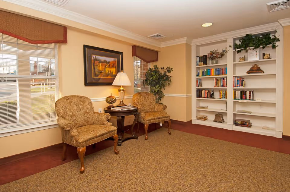 A cozy sitting area with two upholstered chairs, a side table and lamp, and built-in bookshelves.