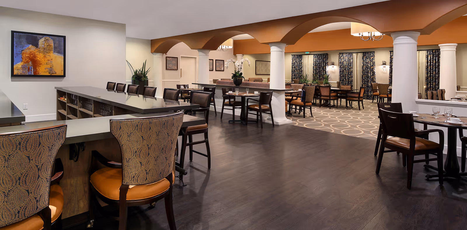 Spacious dining room with a service counter/bar, multiple tables and chairs, decorative columns and archways, and warm lighting.