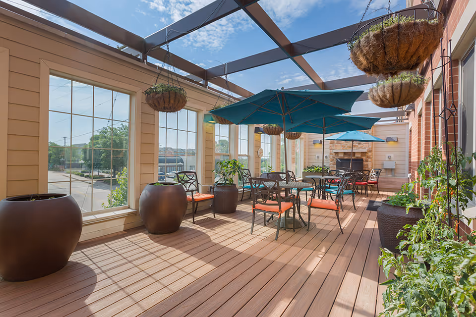 Covered outdoor patio with tables and umbrellas, hanging baskets, and potted plants under a pergola.