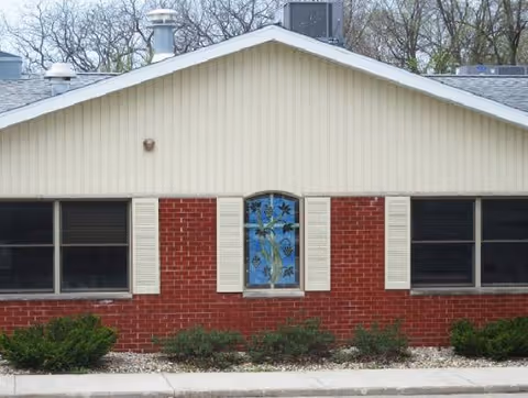 Front exterior of a single-story brick building with beige siding and shrubs.