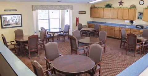 Interior dining room with round tables, chairs, and a cabinet-lined back wall.