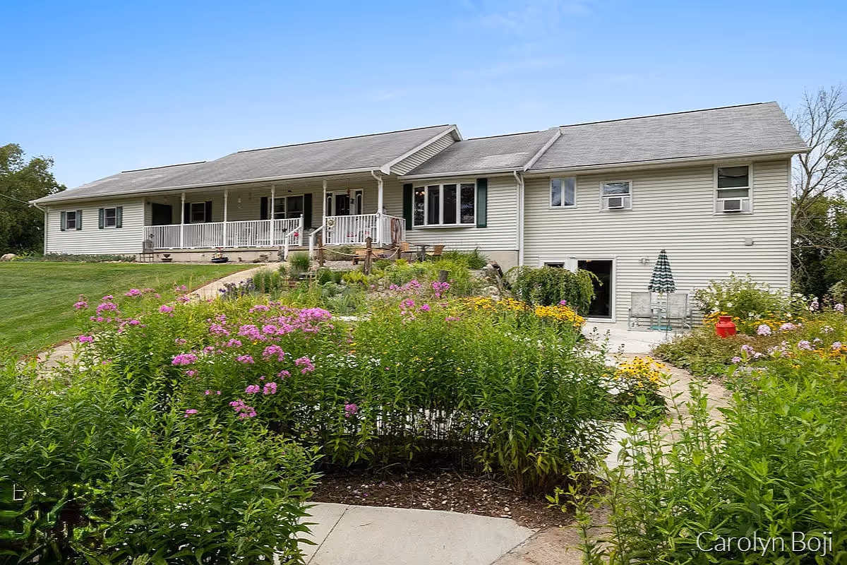 Single-story light-colored residential building with a covered front porch and a colorful flower garden in the foreground.
