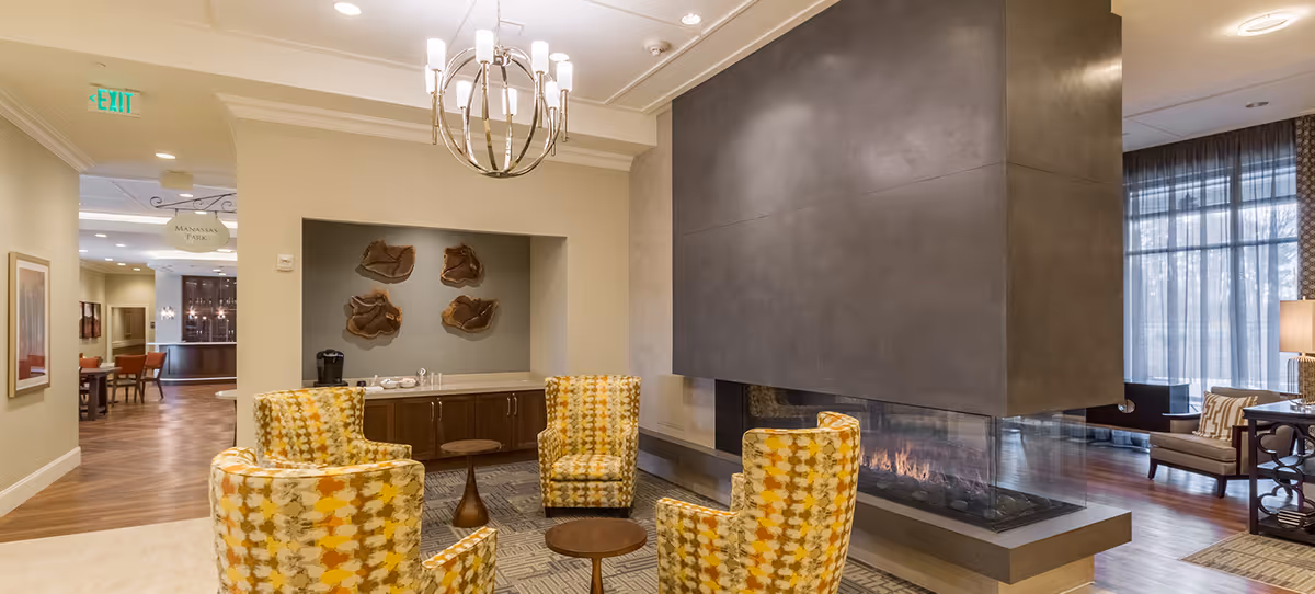 Well-appointed communal lounge with patterned armchairs arranged around a double-sided fireplace and a chandelier.