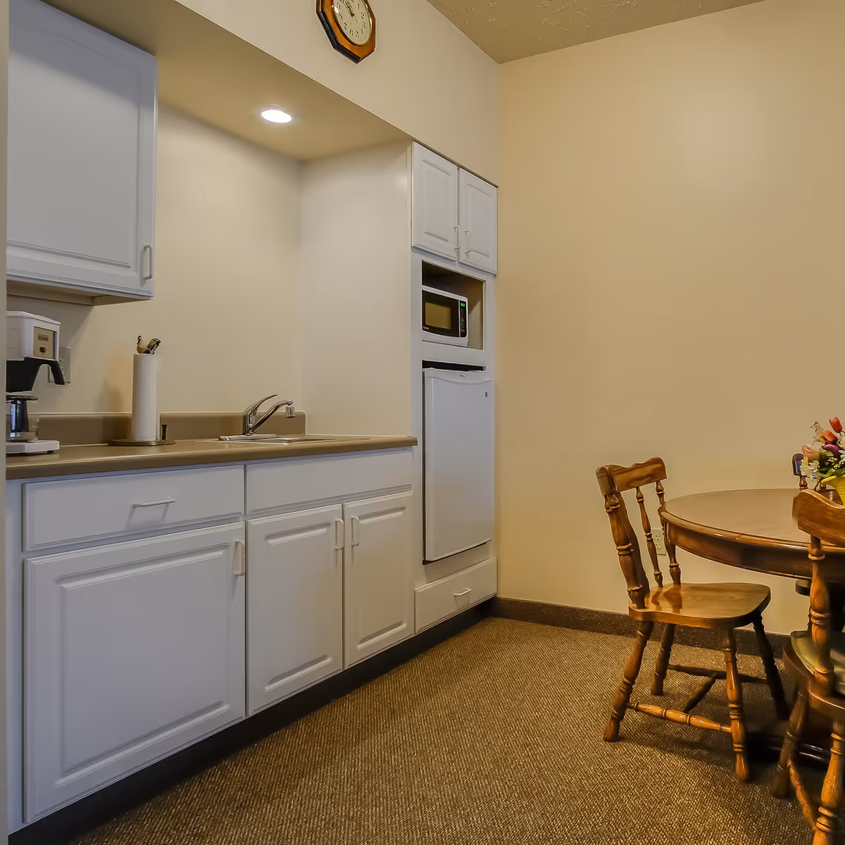 Small kitchenette with white cabinets, a sink, microwave and a round wooden dining table with chairs.