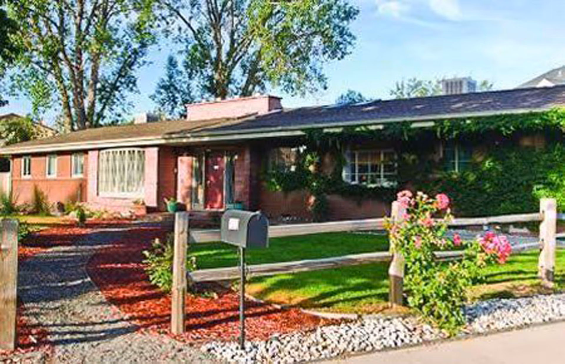 Single-story brick ranch-style building with a front yard, mailbox, wooden fence and flowering shrubs.