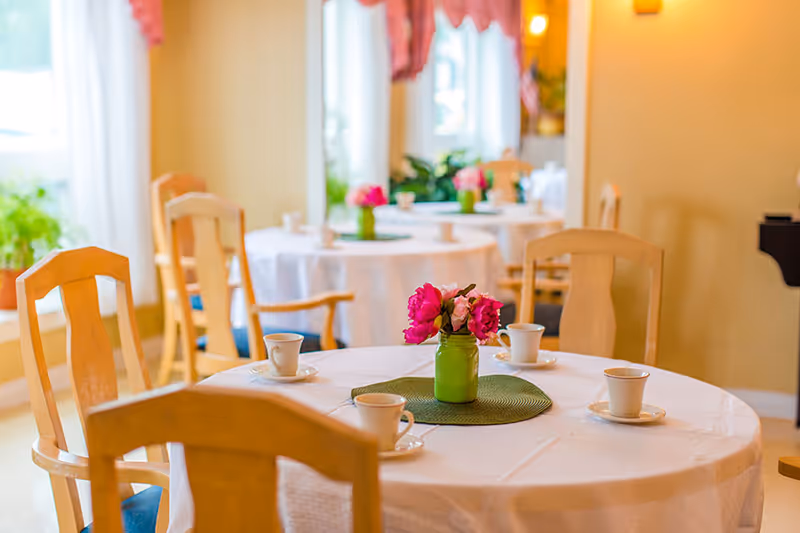 Round dining table set with teacups and a small vase of pink flowers in a bright dining room.